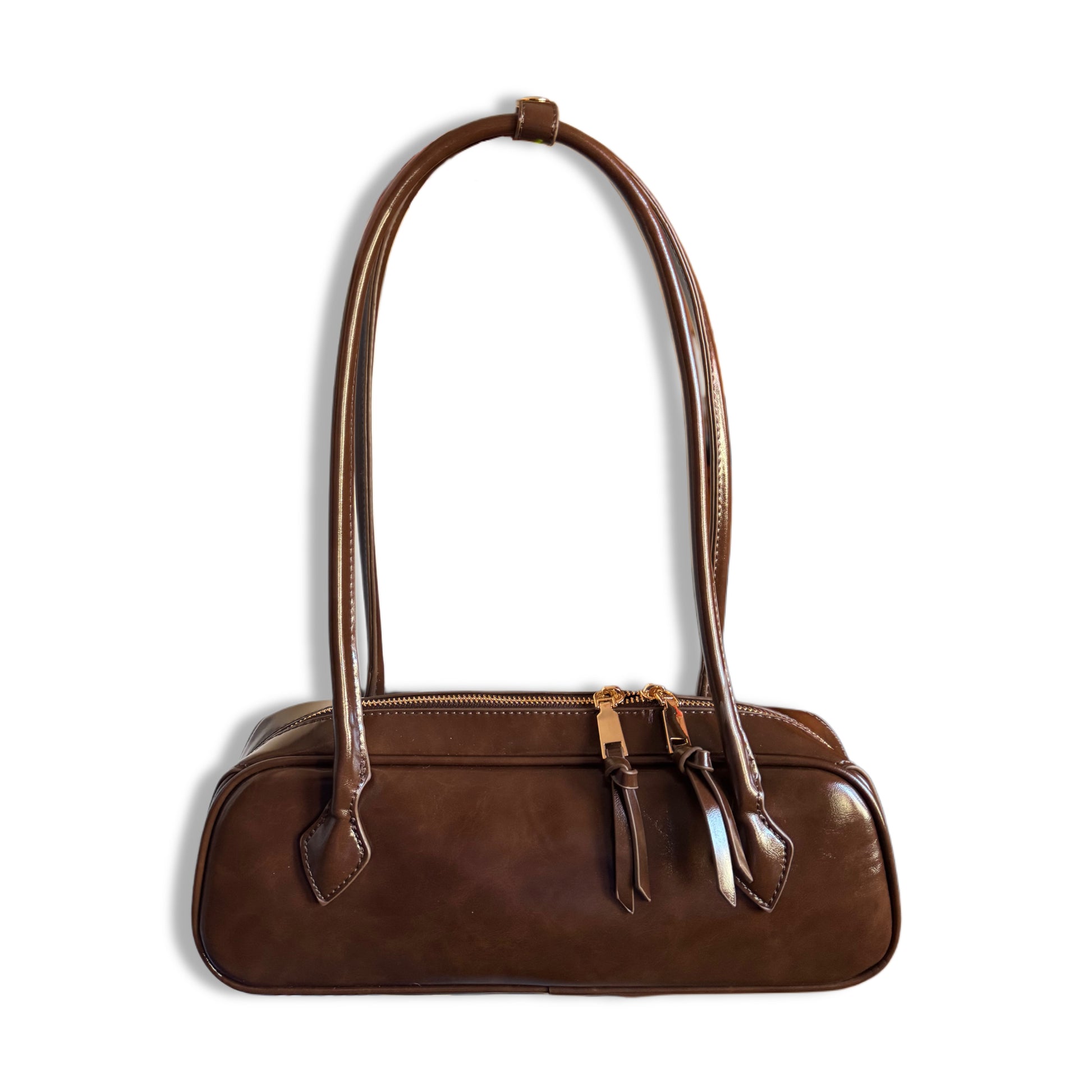 Borsa realizzata in una splendida similpelle lucida, color marrone. Questa borsa a bauletto allungato si distingue per il suo look retrò e sofisticato. Uno stile vintage-chic intramontabile che unisce la praticità dei lunghi manici alla sicurezza di una cerniera superiore.